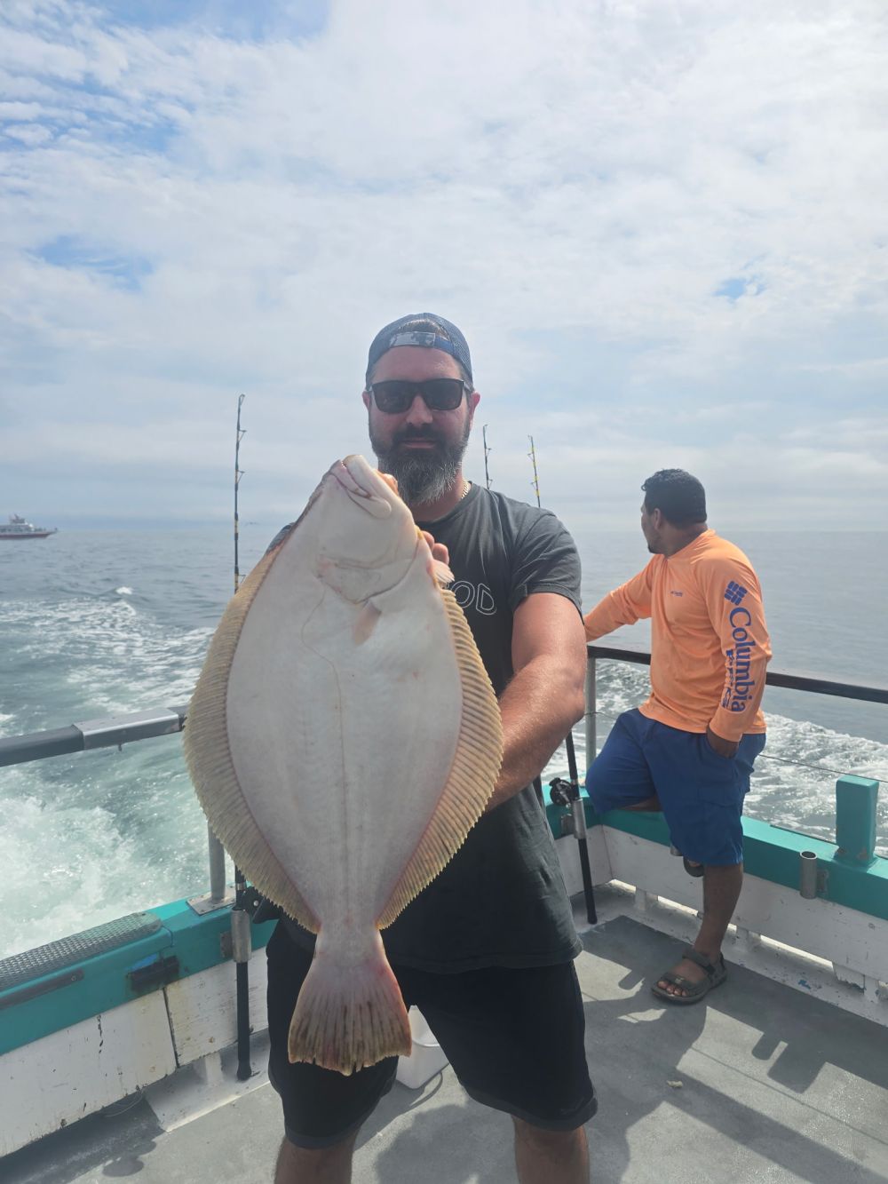 Person holding a large flatfish on a boat with another person in the background.