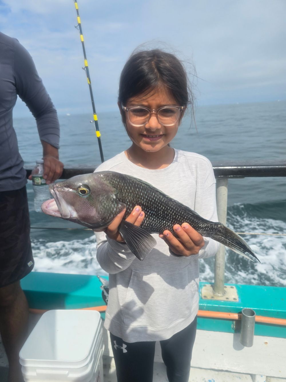 Child holding a fish on a boat with ocean in the background.