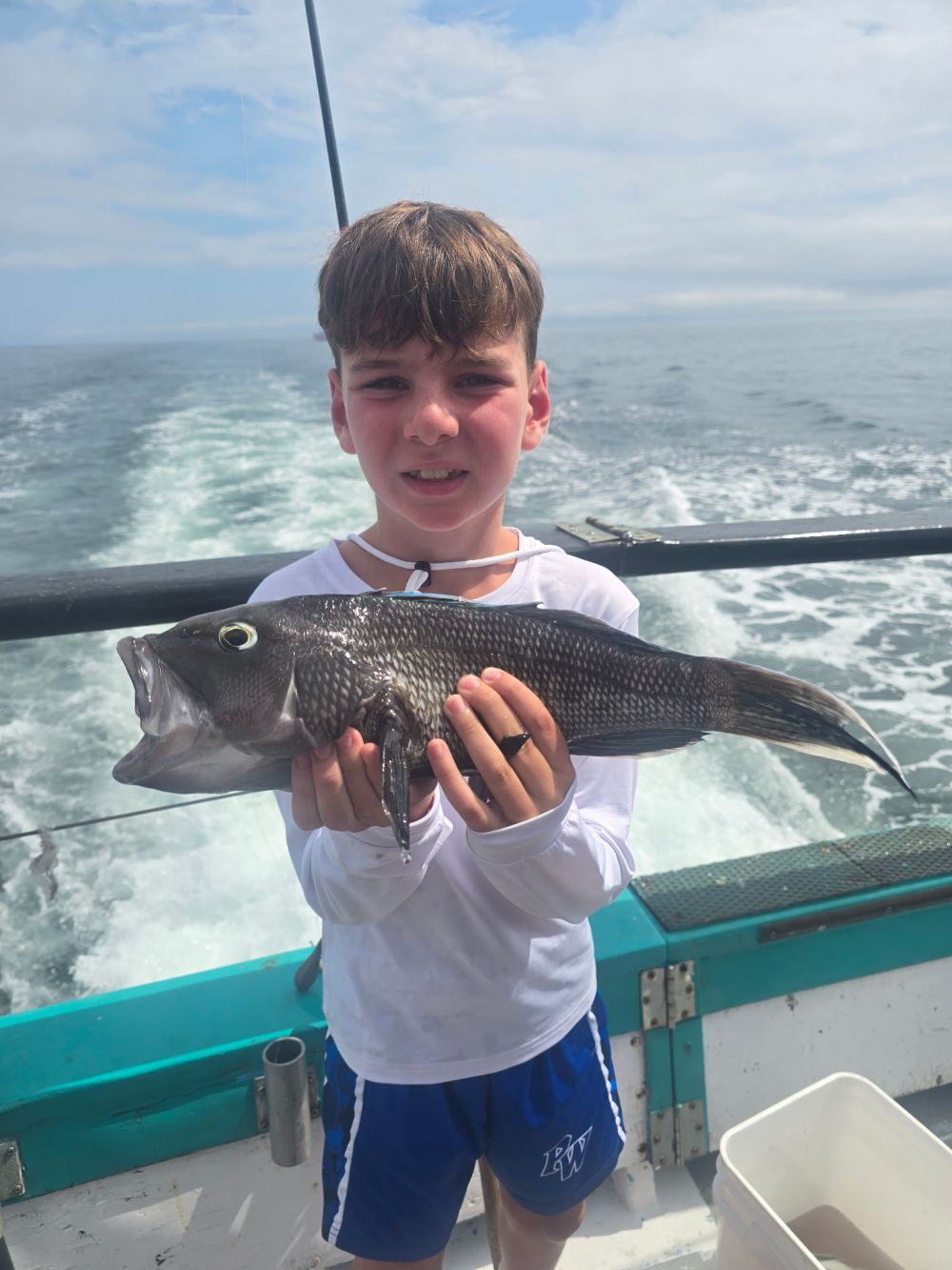 Boy holding a fish on a boat with ocean in the background.