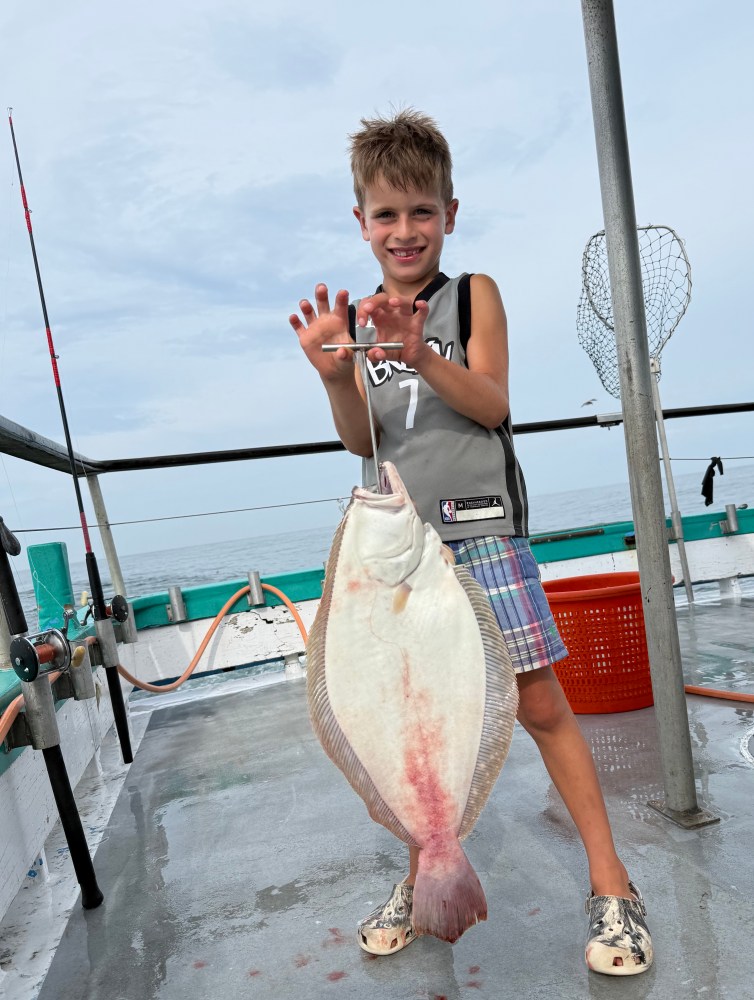 Boy proudly holding a large fish on a boat deck with a fishing net nearby.