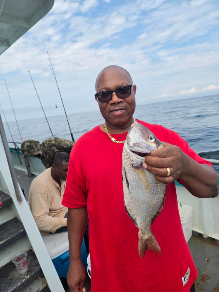 Man in red shirt holds a fish on a boat with ocean in background.