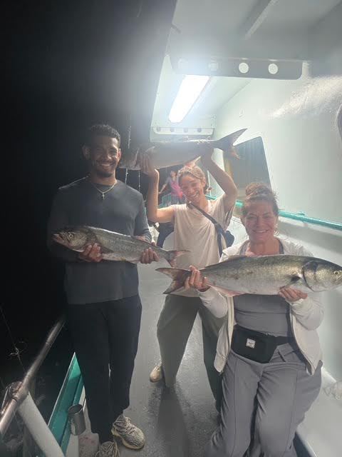 Three people on a boat holding large fish, smiling at night.