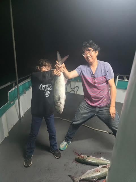 Two people proudly holding a large fish on a boat at night.
