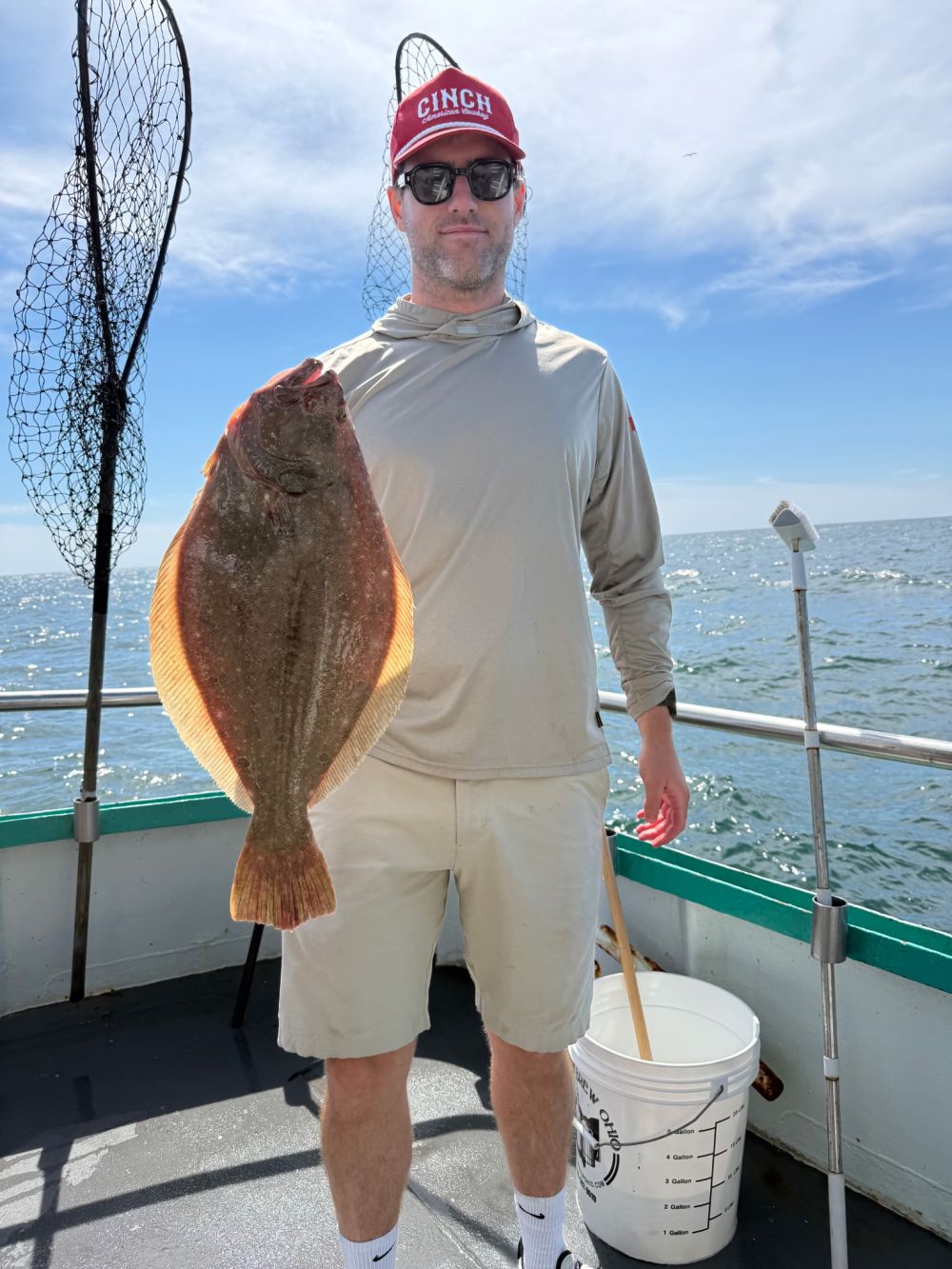 Person on boat holding a flat fish with a net and bucket nearby.