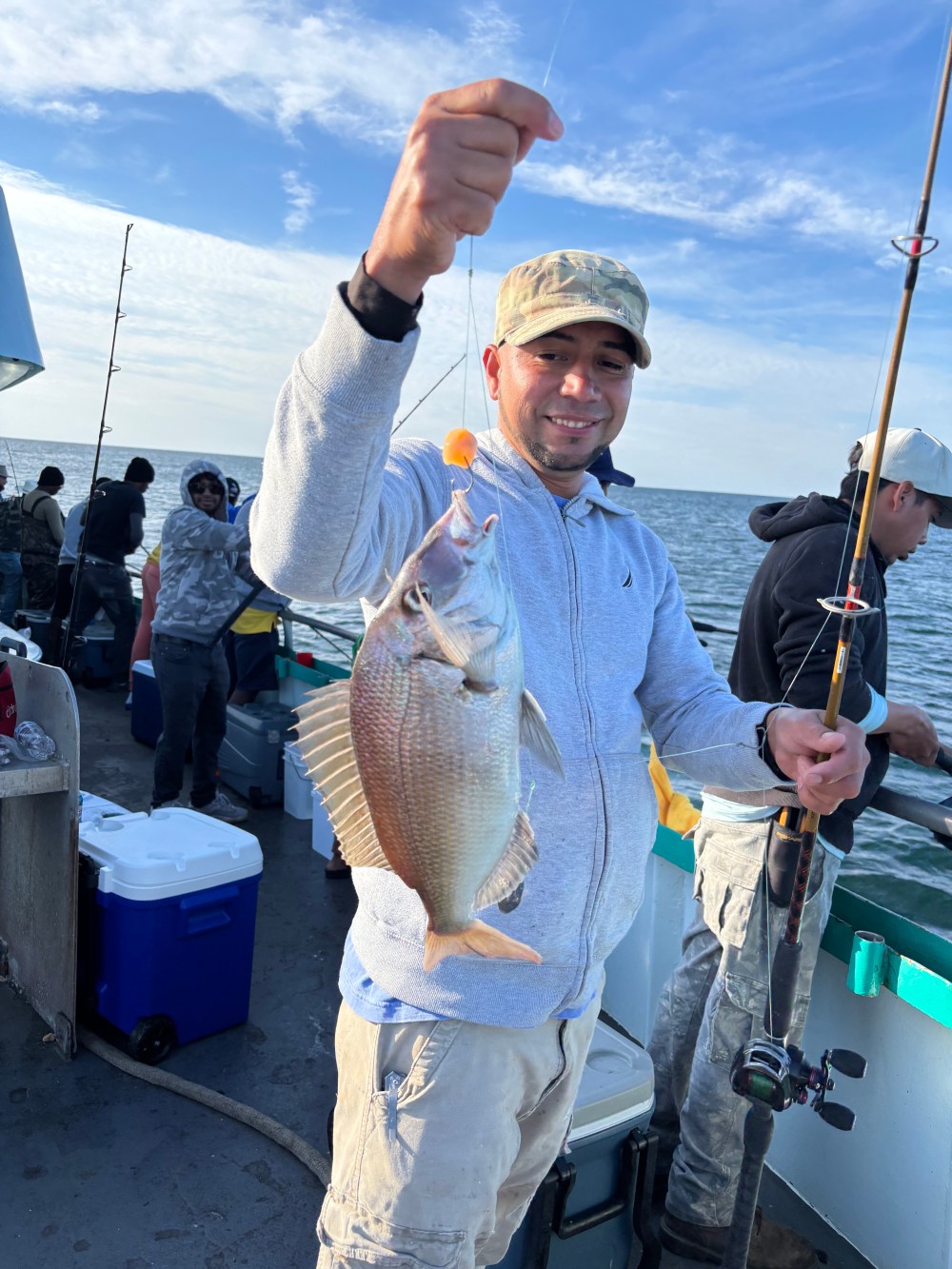 Person holding a fish on a boat with others around, ocean in the background.