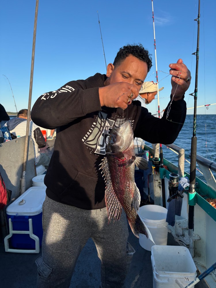 Man holding a large fish on a boat, with fishing rods in the background.