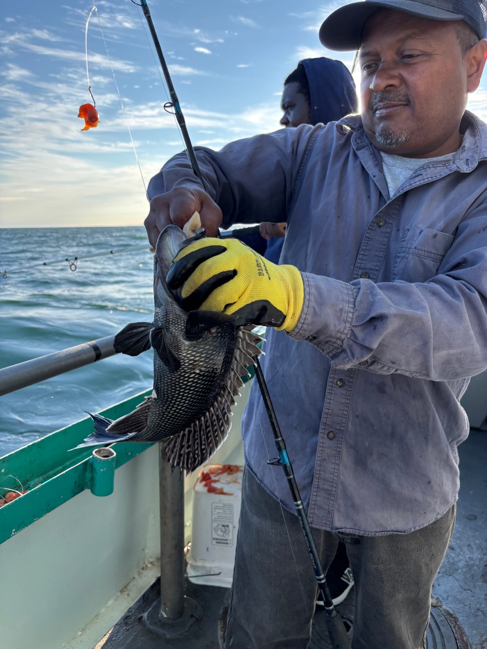 Man holding a fish on a fishing boat under a cloudy sky.