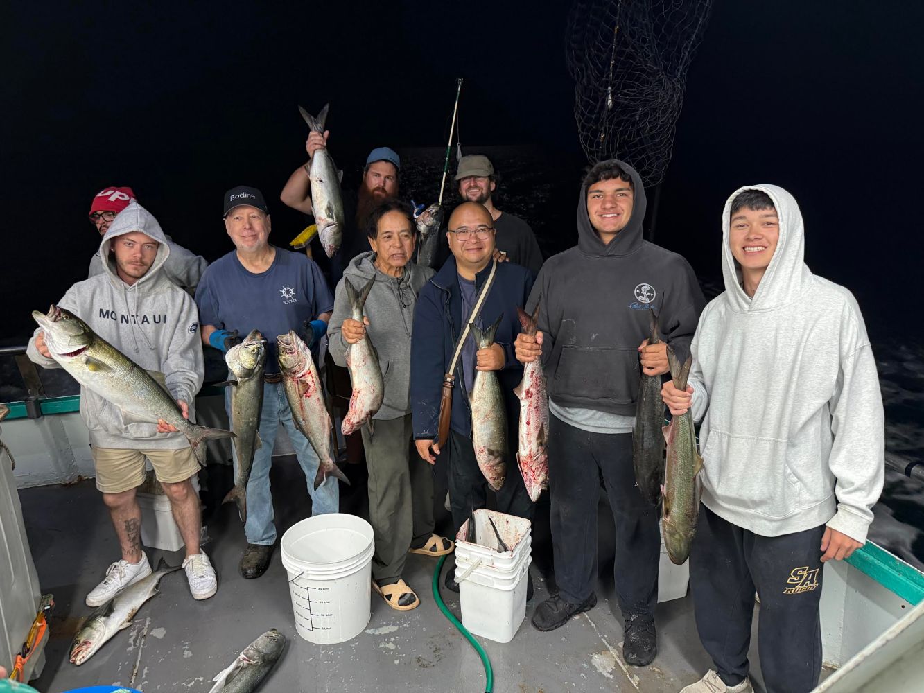 Group of people on a boat displaying their caught fish at night.