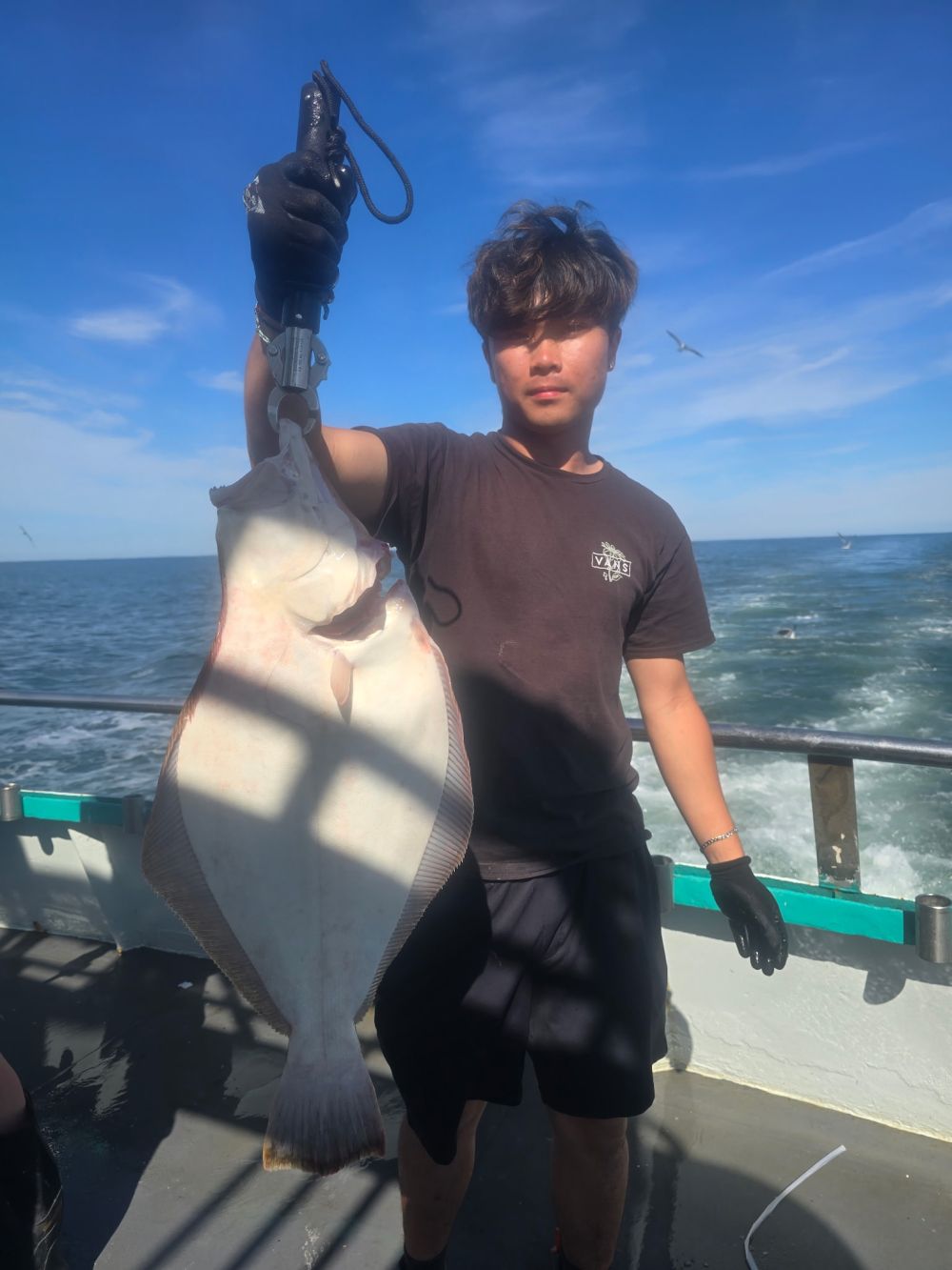 Person holding a large fish on a boat under a clear sky.