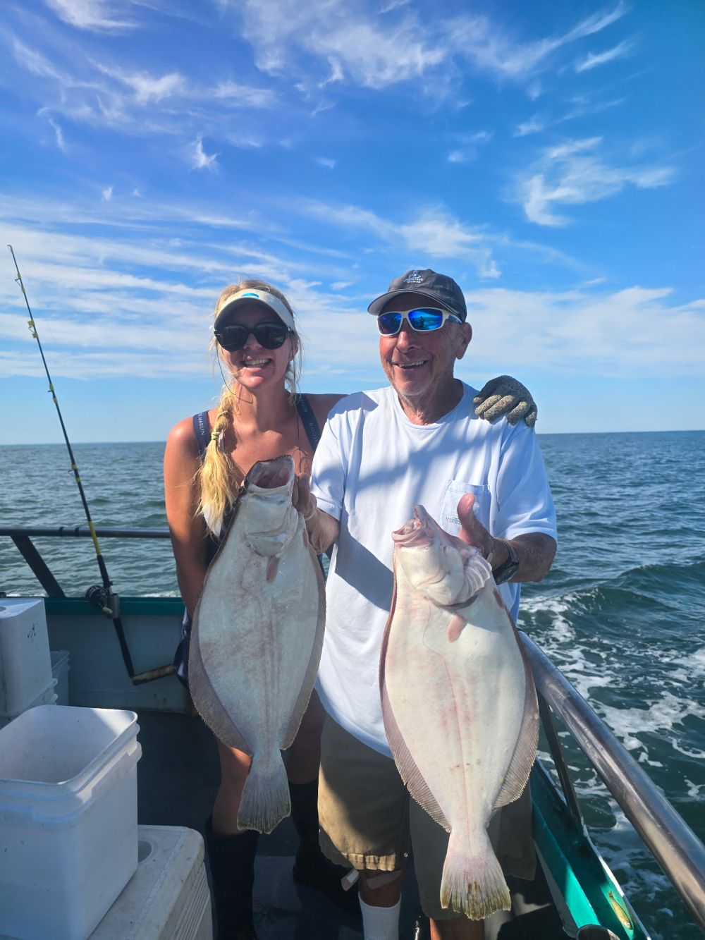 Two people holding large fish on a boat under a blue sky.