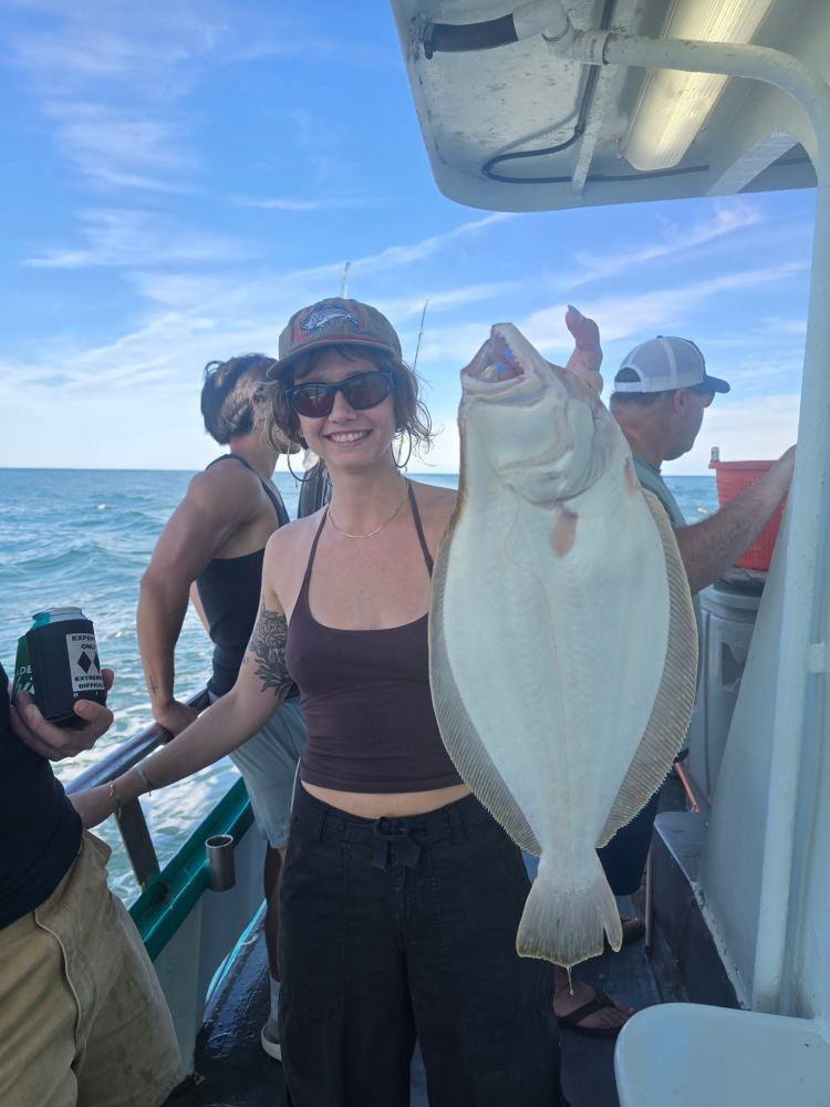 Person holding a large fish on a boat with others and ocean in background.
