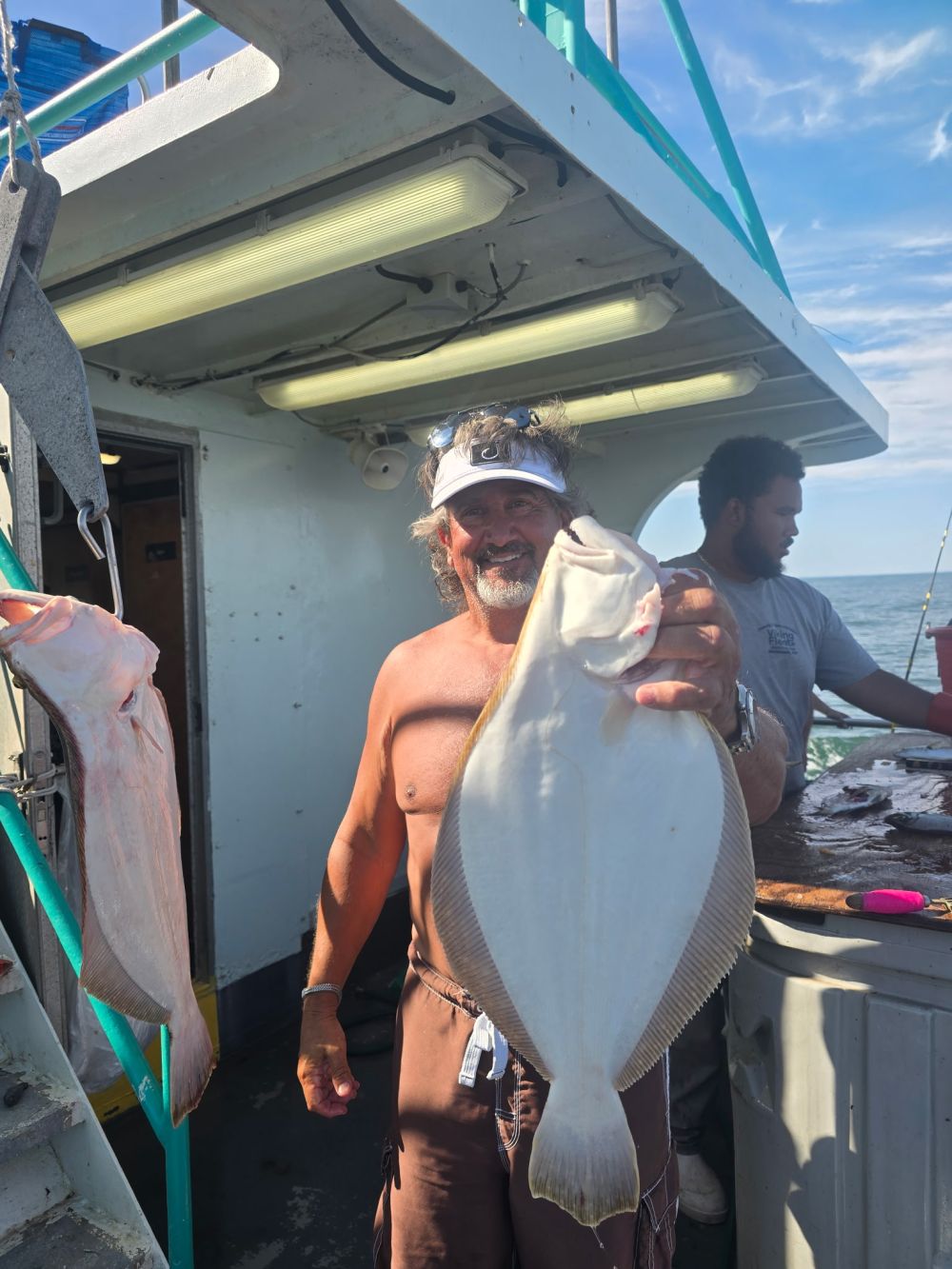 Man holding a large fish on a boat with another man behind him.