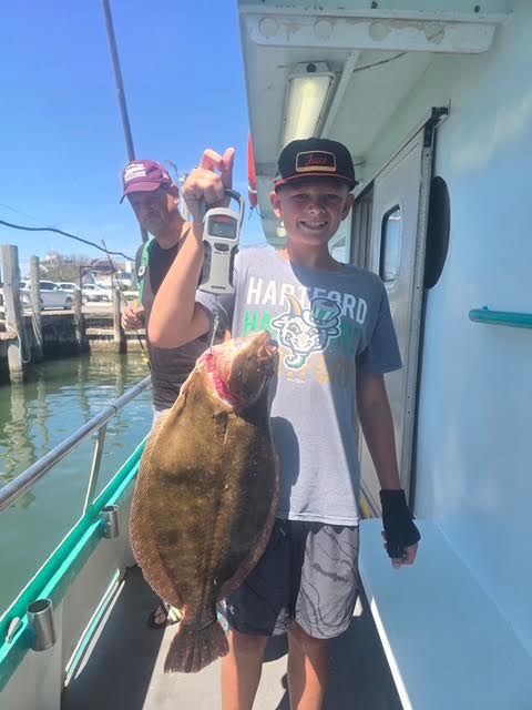 Boy on boat holding a large flat fish with a man smiling in the background.