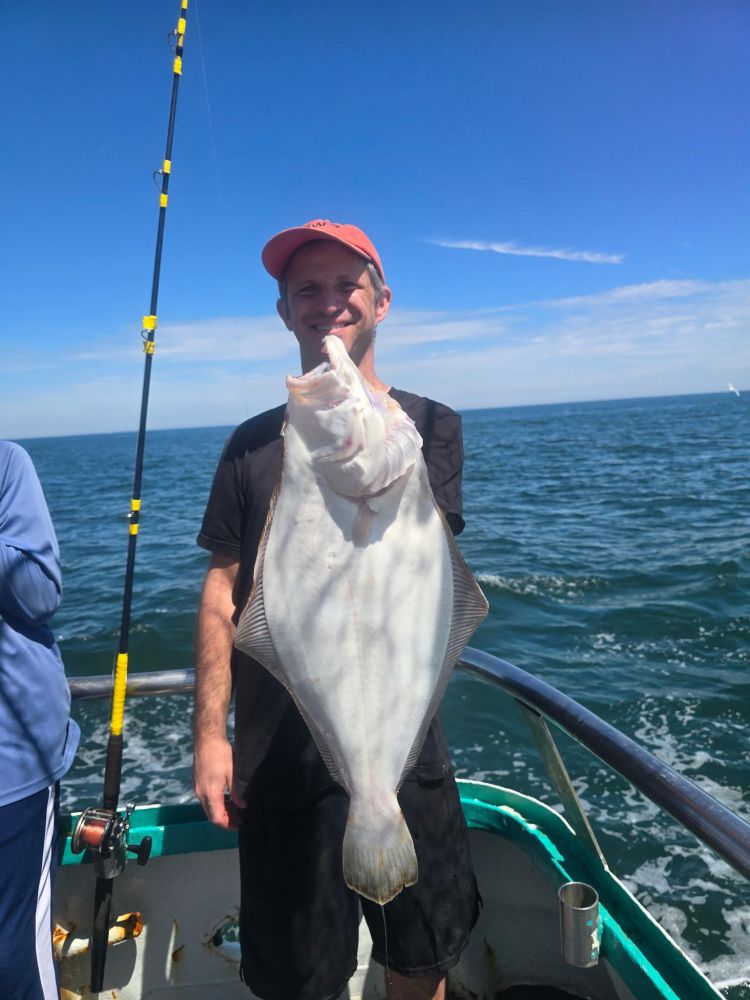 Person holding a large fish on a boat in the ocean under a clear blue sky.