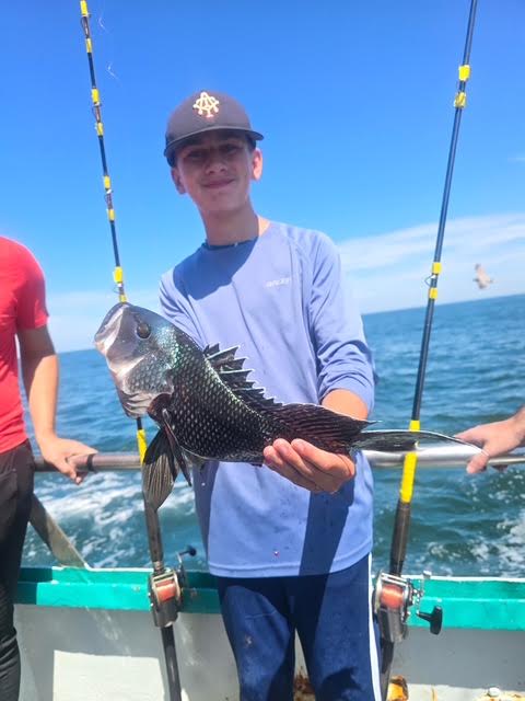 Boy holding a fish on a boat with fishing rods and ocean in the background.
