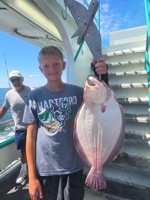 Boy holding a large fish on a boat, smiling beside a man near stairs.