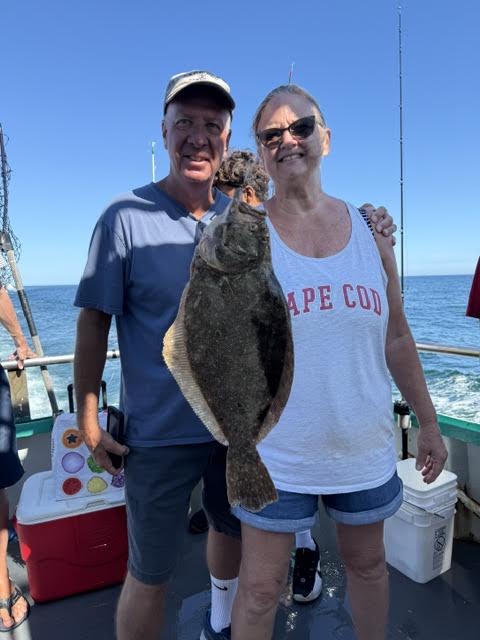 Two people on a boat holding a large flat fish, with fishing rods in the background.
