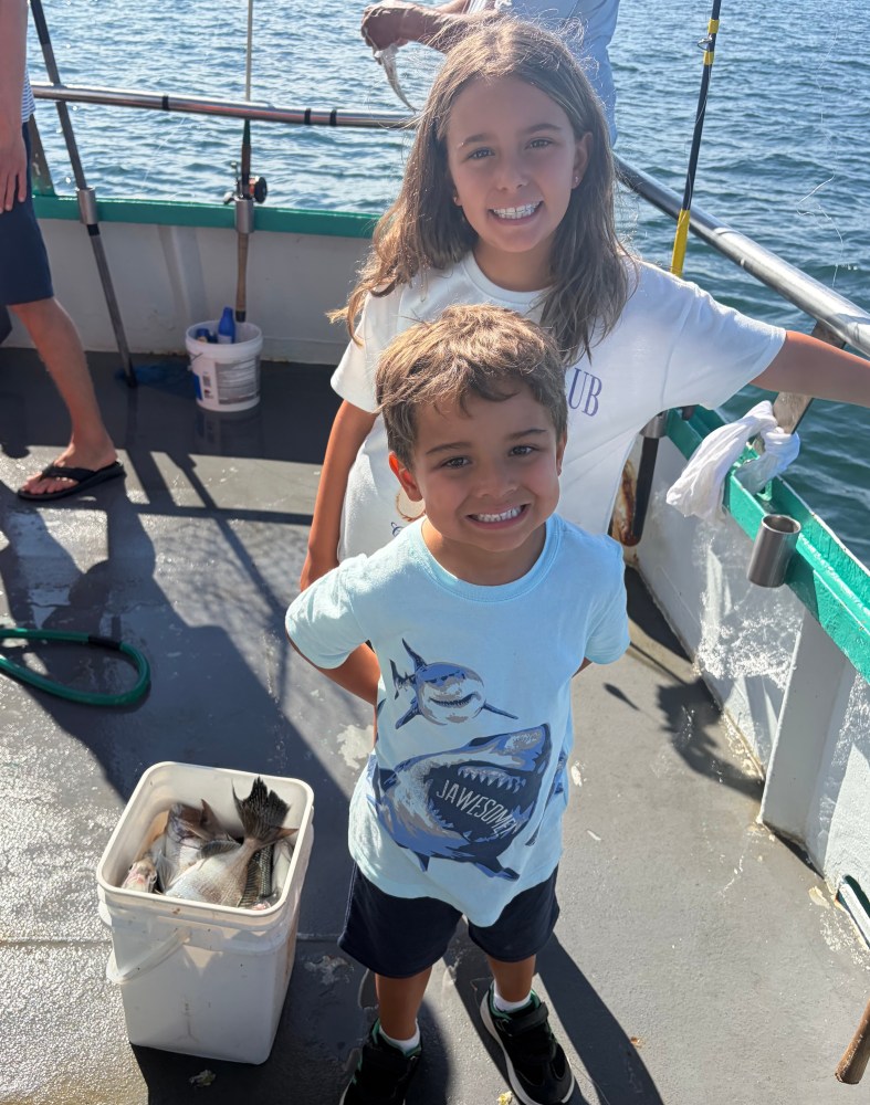 Two smiling children on a boat with a bucket of fish.