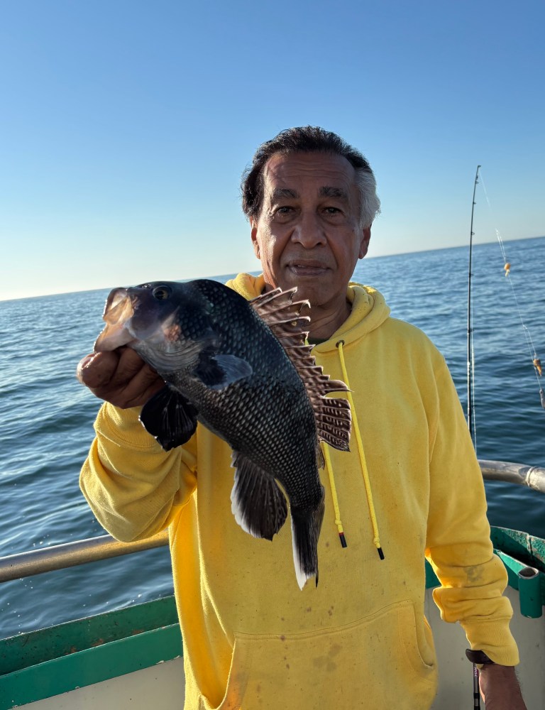 Man in yellow hoodie holding a fish on a boat with the ocean in the background.