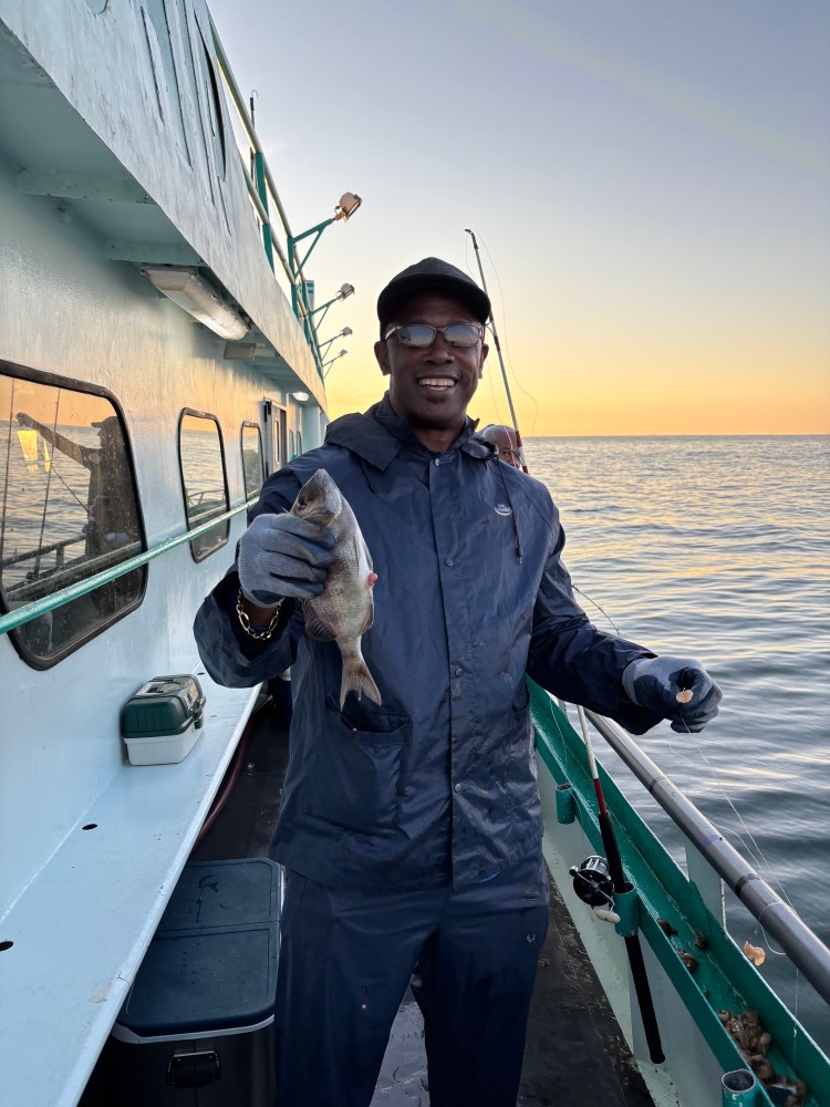 Person on boat holding a fish at sunset.