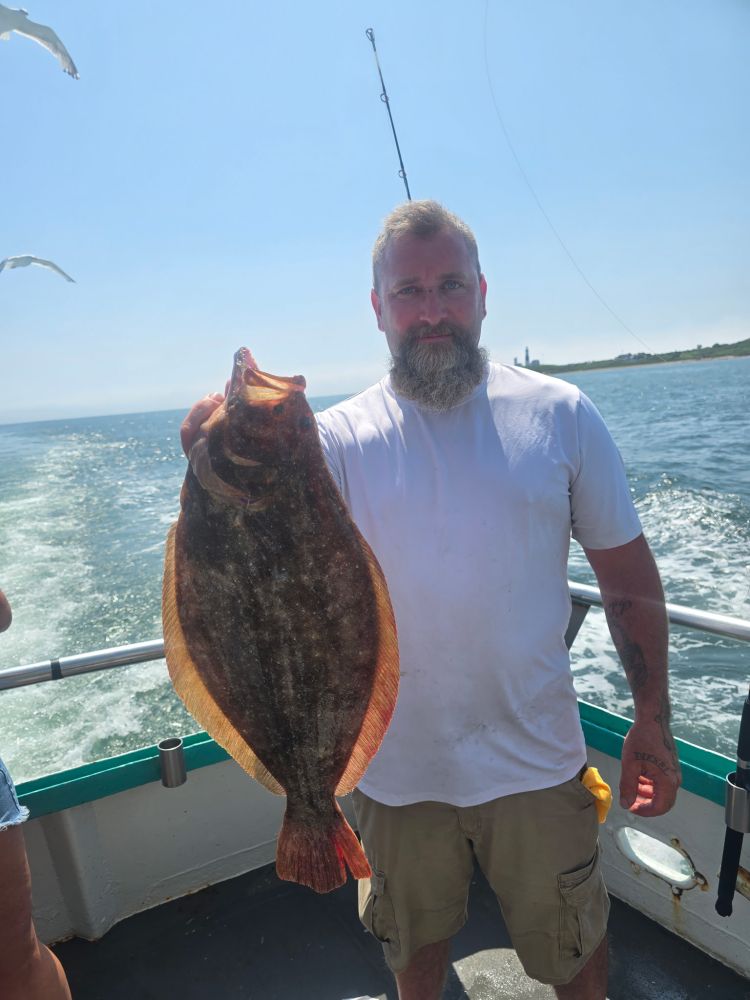 Man holding a large fish on a boat, with ocean and sky in the background.