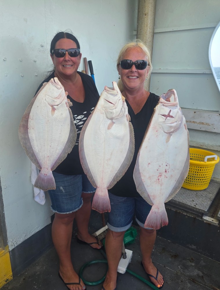 Two women holding large fish on a boat, both wearing sunglasses and smiling.