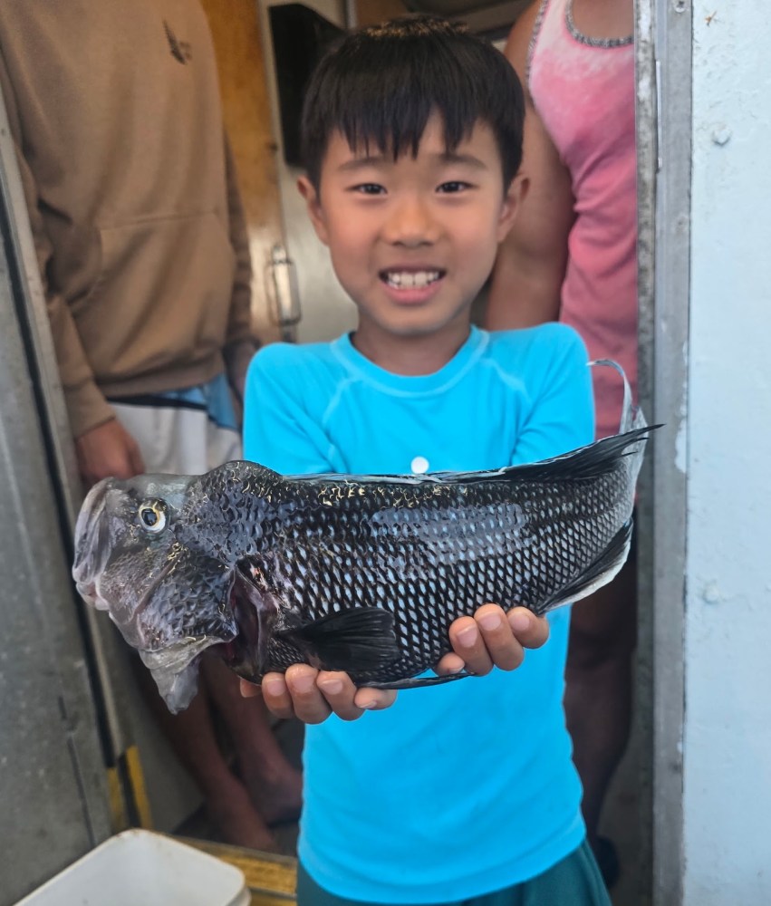 Child holding a large fish with a smile inside a boat cabin.