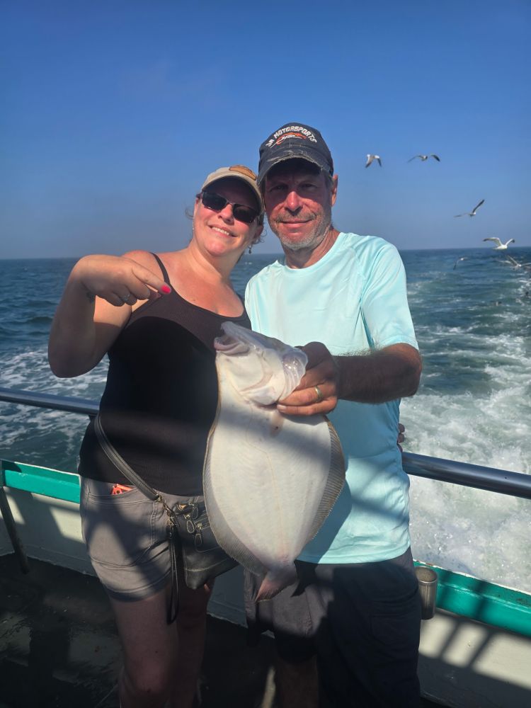 Smiling couple on a boat holding a large fish with seagulls flying nearby.