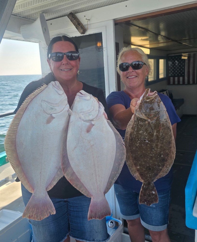 Two women smiling, holding large fish on a boat.