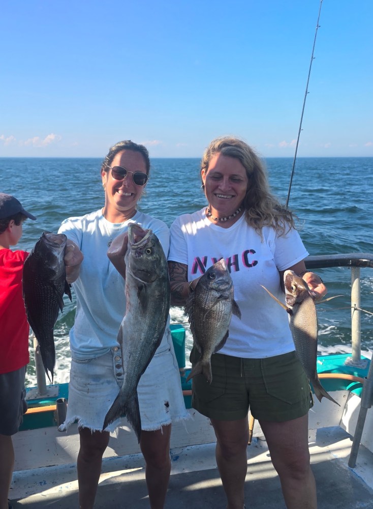 Two people holding fish on a boat with ocean in the background.