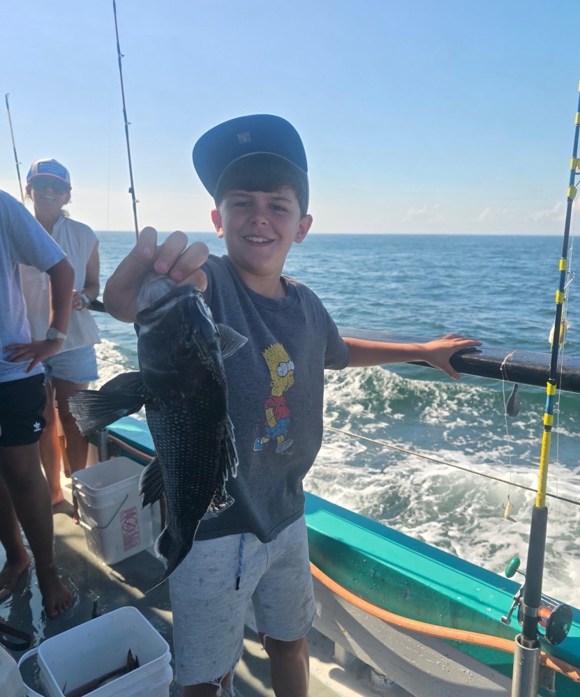 Boy holding a fish on a boat with ocean in background.