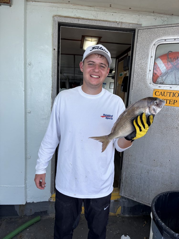 Person in white shirt holding a fish on a boat, smiling.