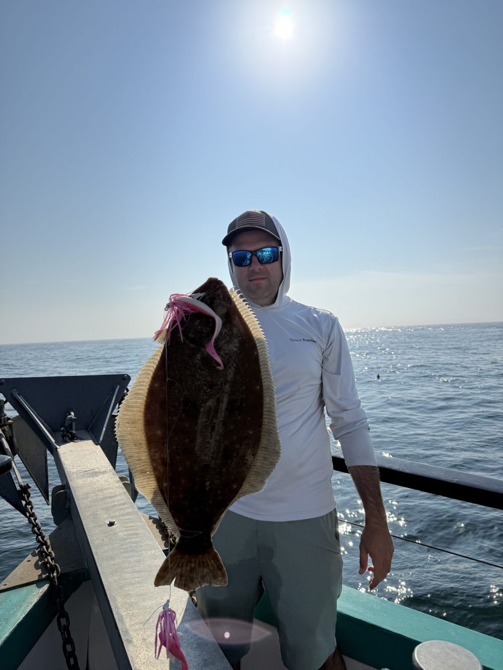 Person on boat holding a large fish against a sunny sky.