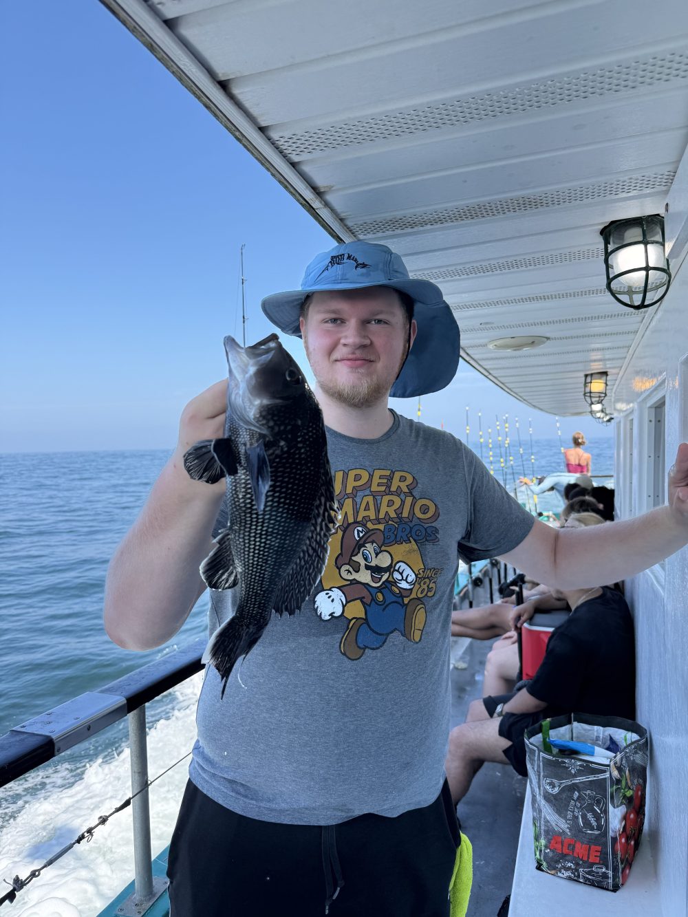 Person holding a fish on a boat, wearing a hat and Super Mario shirt.