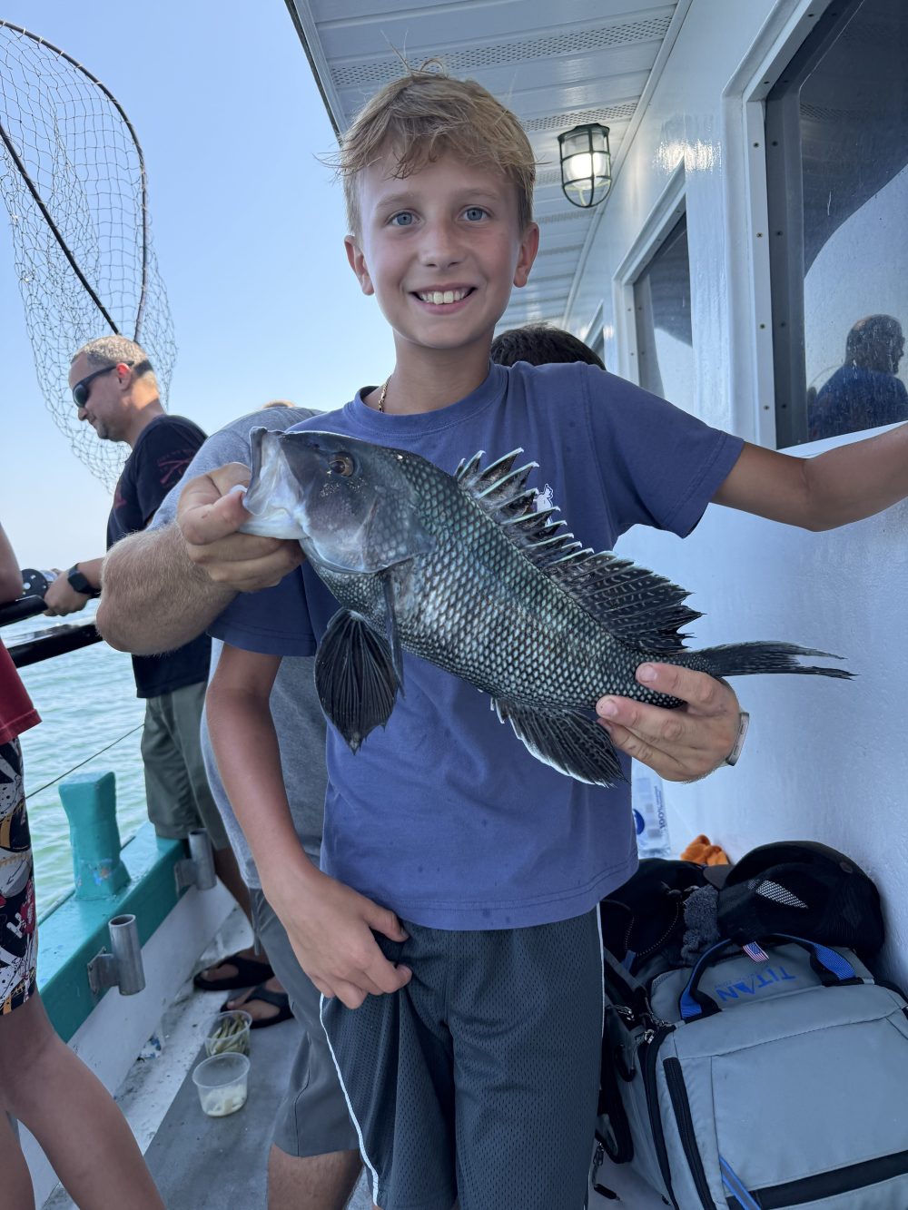 Boy on boat proudly holding a freshly caught fish.