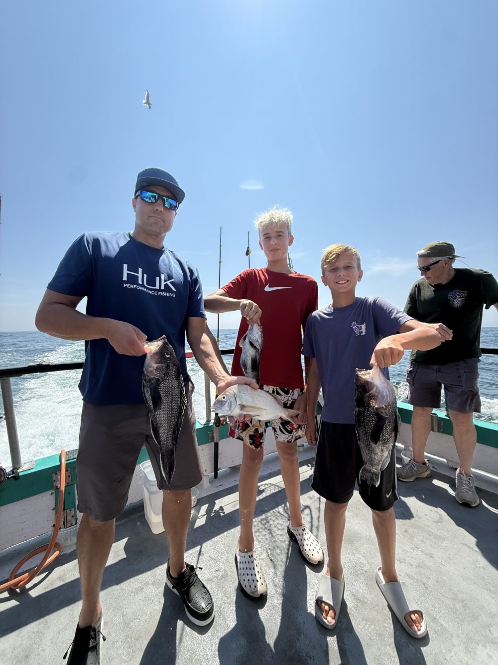 Group of four people on a boat holding fish, clear sky above.