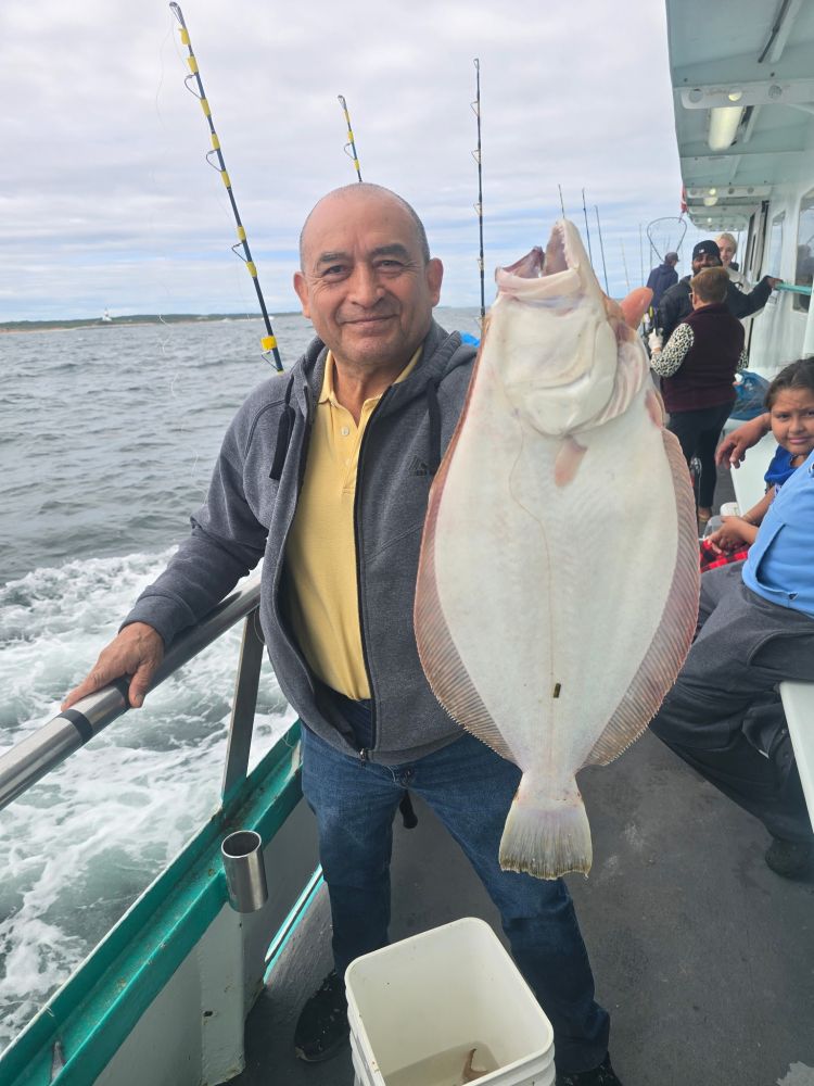 Man on boat holding a large fish, with ocean in the background.