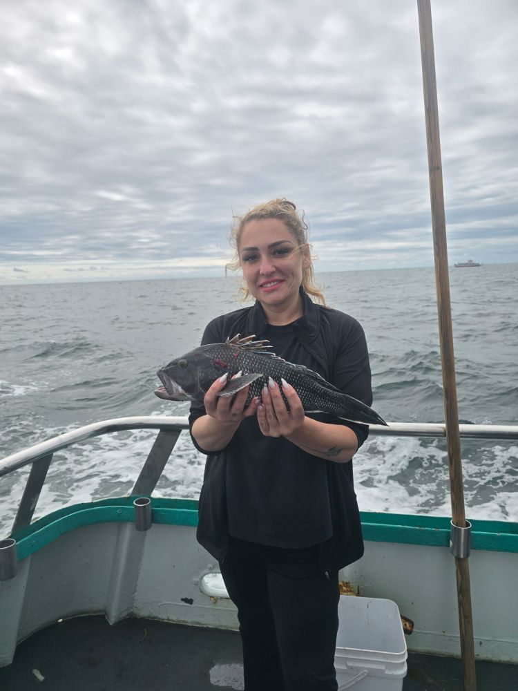 Person holding a fish on a boat with ocean in background.