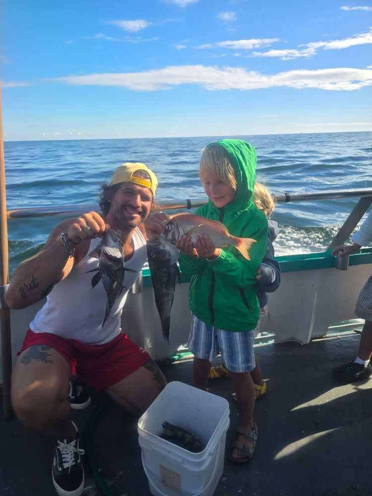 Adult and child proudly holding fish on a boat with ocean backdrop.