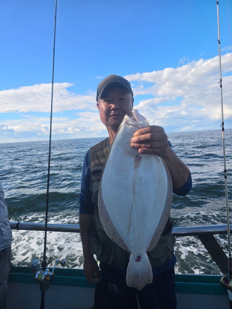 Person holding a large fish on a boat with ocean and sky background.