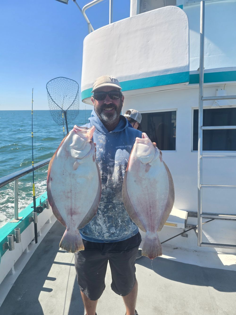 Man on boat holding two large fish with ocean in background.