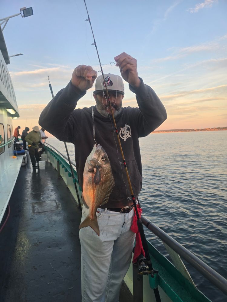 Man holding a caught fish on a boat during sunset.