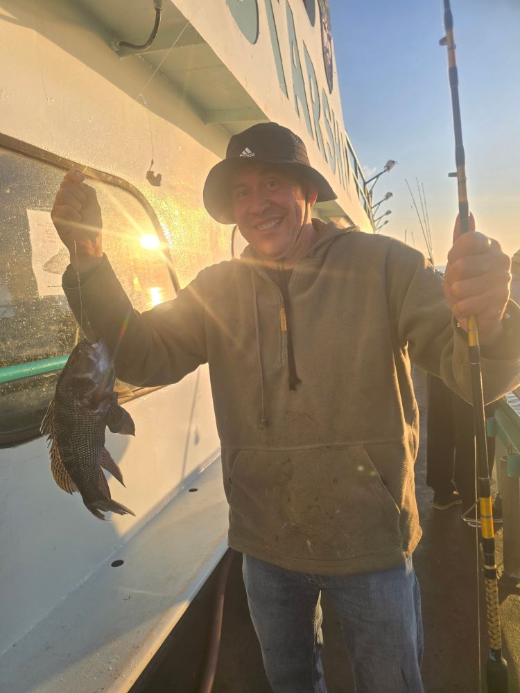 Man holding a fishing rod and a fish on a boat at sunset.