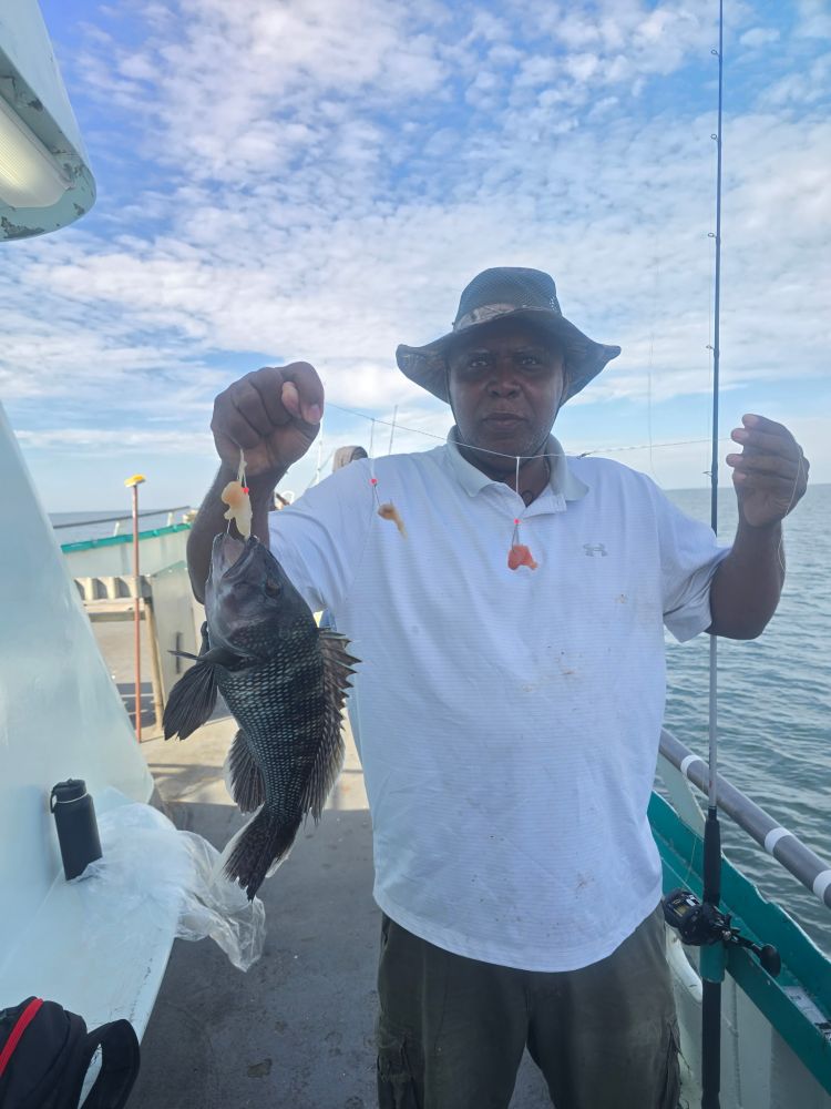 Man on boat holding a fish caught on a line, under a partly cloudy sky.