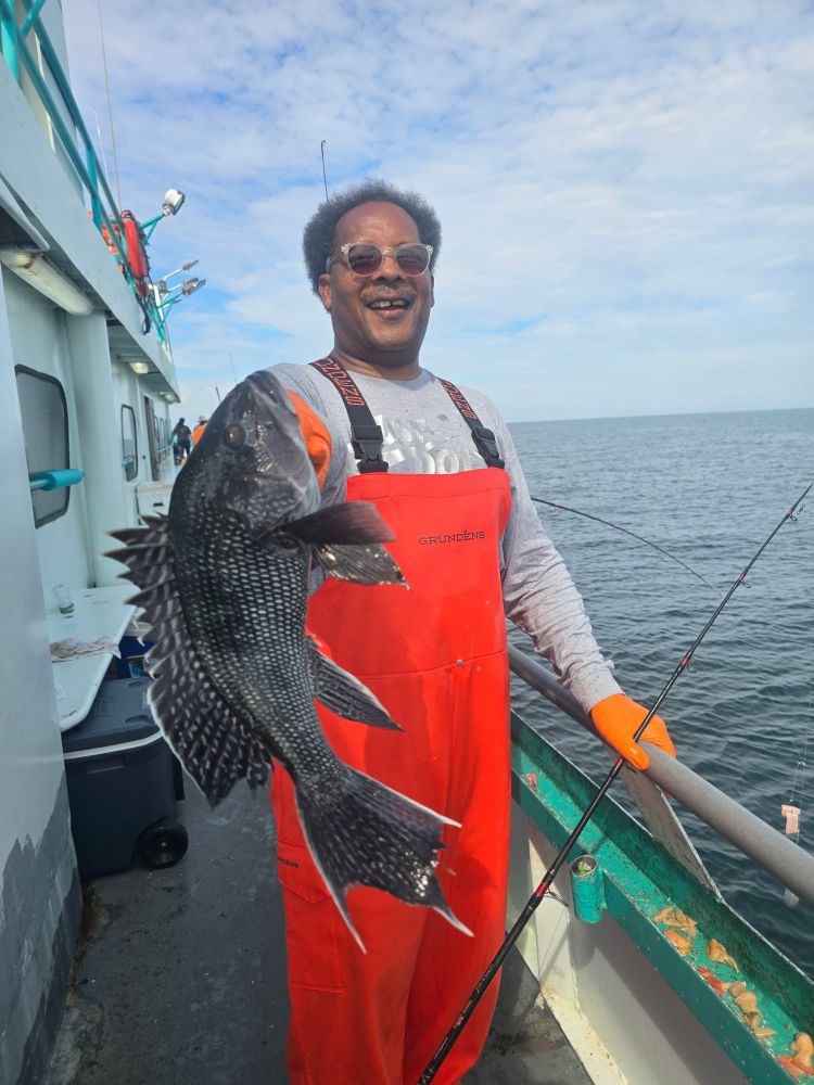 Person in orange coveralls holds a large fish on a boat at sea.