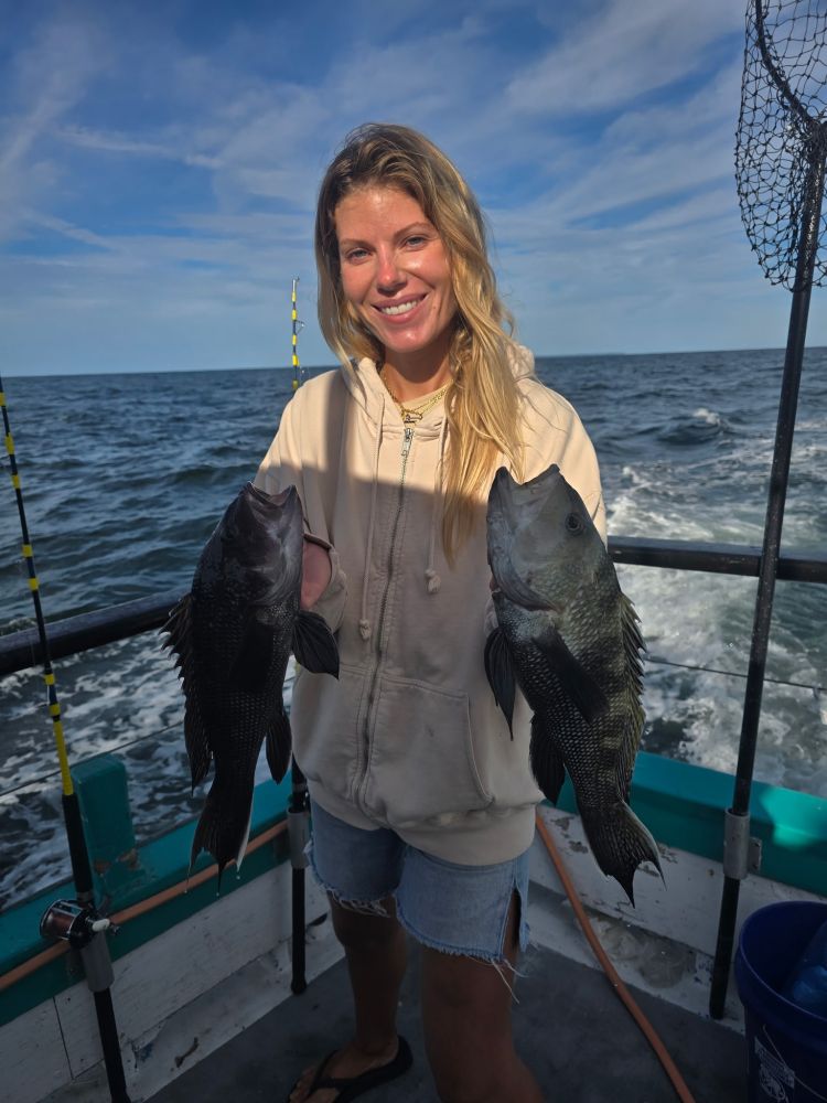 Woman on boat holding two fish with ocean backdrop.