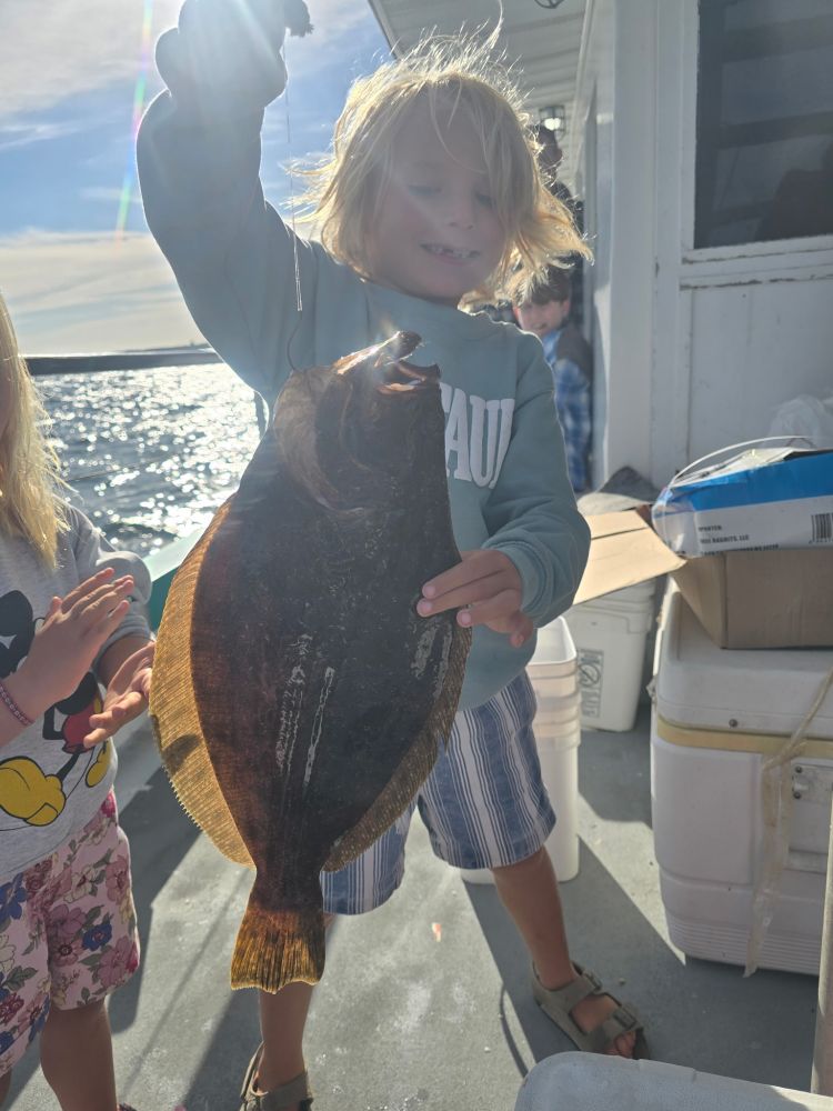 Child holding a large fish on a boat with ocean in the background.