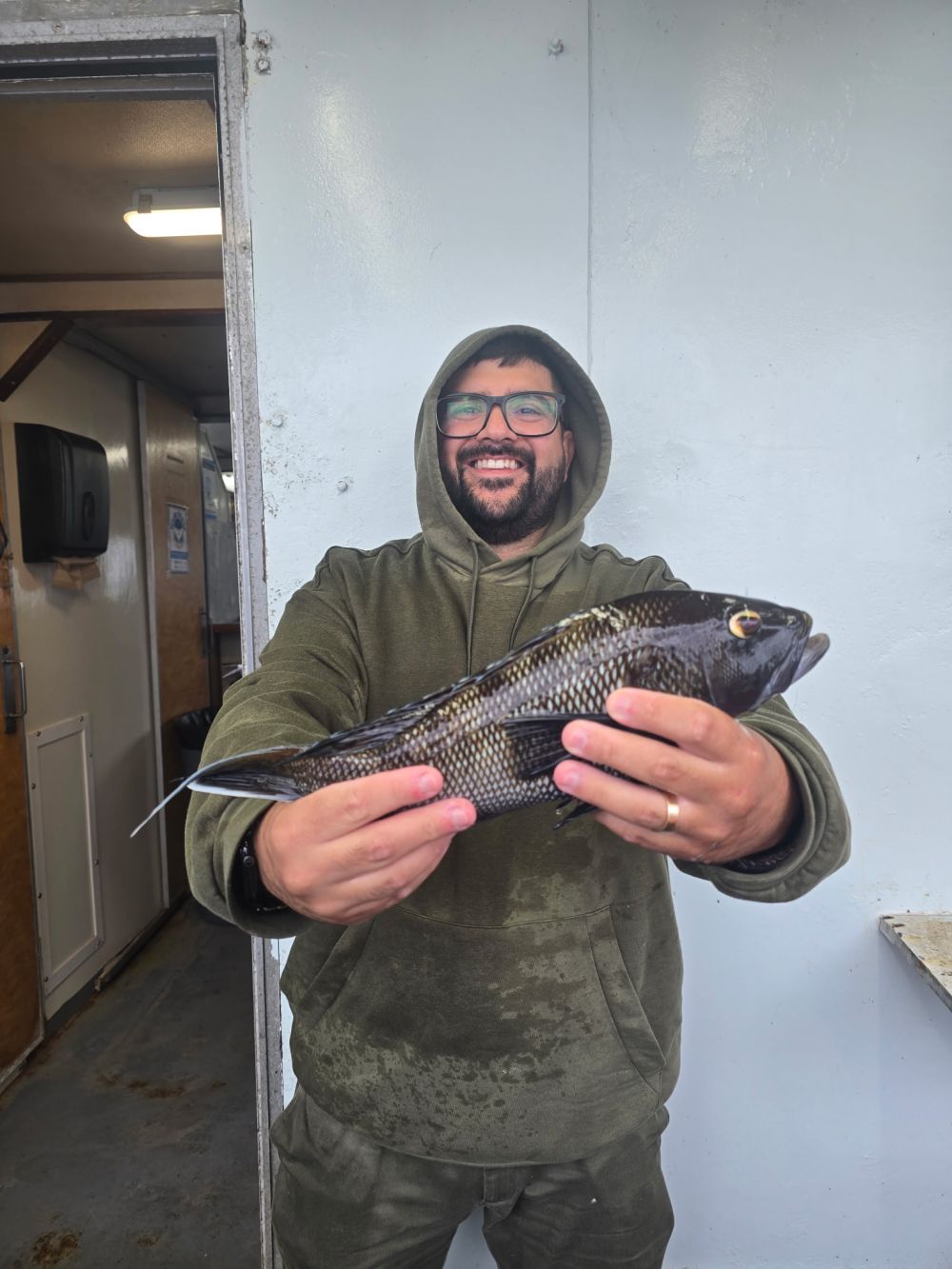 Person in a hoodie proudly holding a fish on a boat.