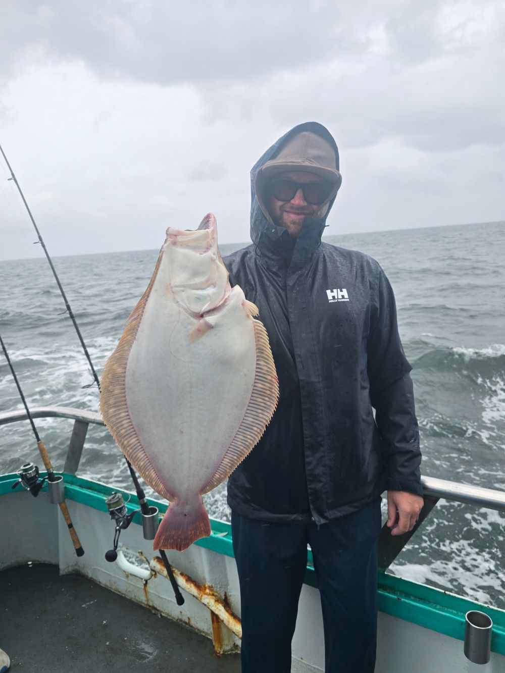 Person in rain gear holding a fish on a boat in cloudy weather.