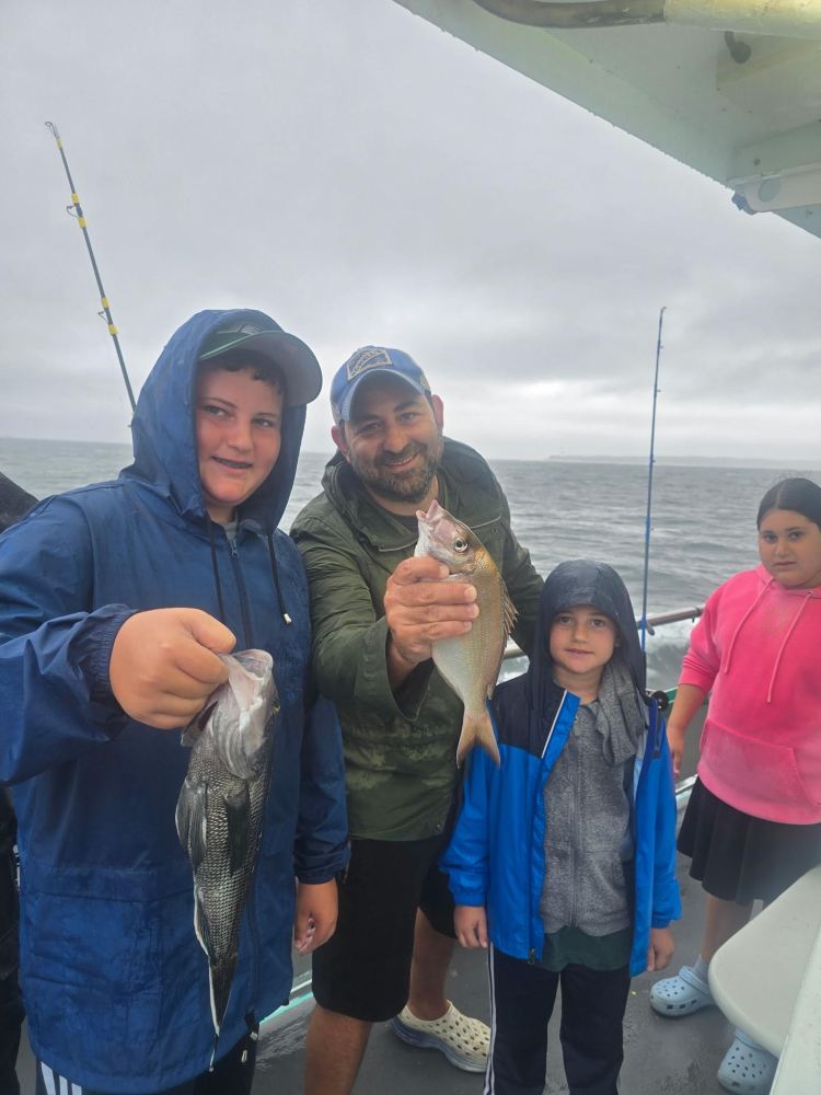 Group on a boat holding caught fish on a cloudy day.